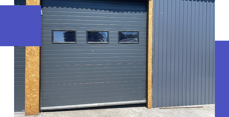 Ciemnoszara brama garażowa z poziomymi panelami, wyposażona w trzy prostokątne okienka w górnej części.
